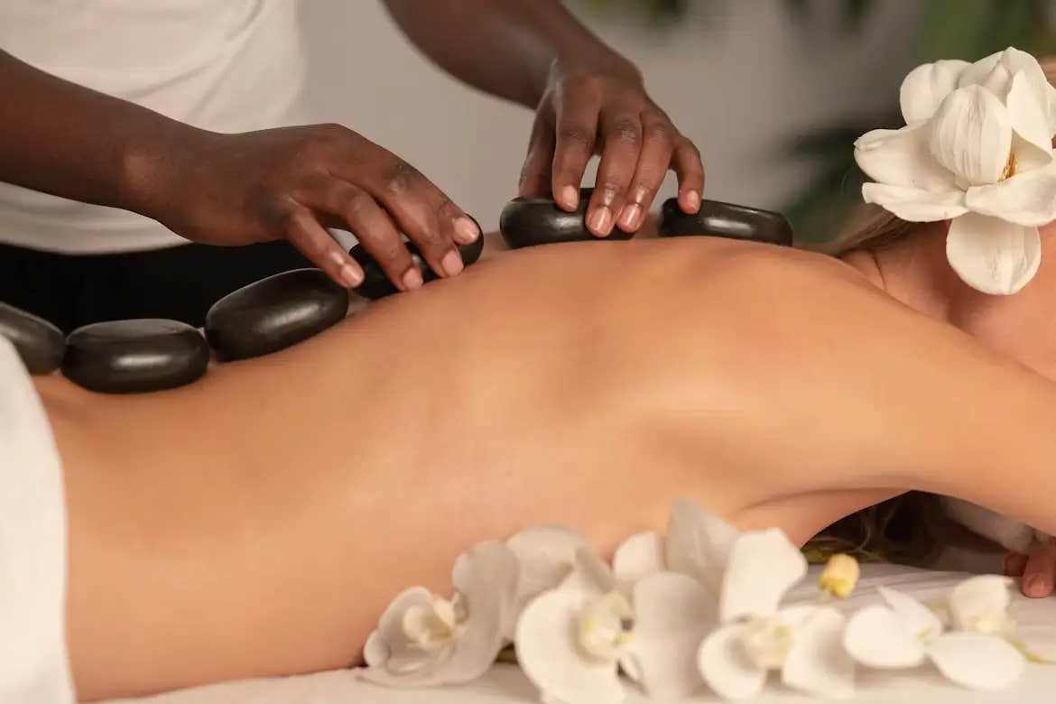 A person receiving a calming hot stone massage on their back, surrounded by white orchid flowers—promoting relaxation, stress relief, and nervous system support.
