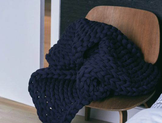 Knitted navy blue weighted blanket on a wooden chair.