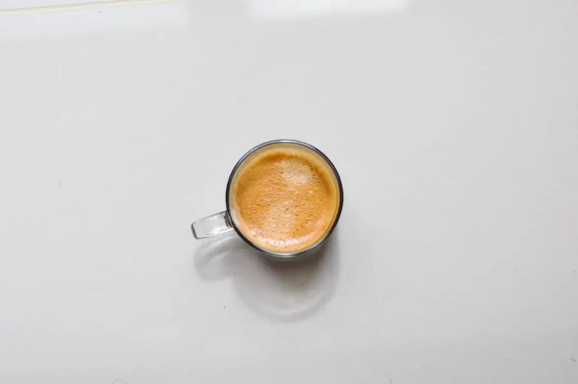 Glass cup of espresso on white surface, top view.