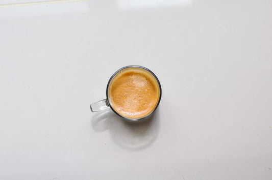 Glass cup of espresso on white surface, top view.