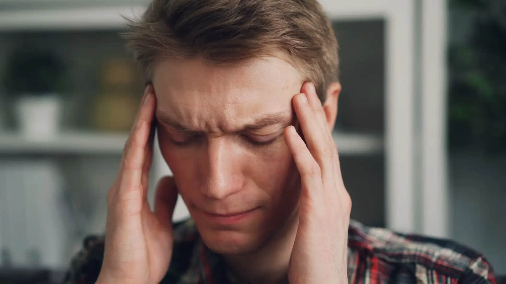 A man holding his head with both hands and eyes closed, appearing to be in discomfort or pain—representing the physical toll that chronic stress can take on the body.