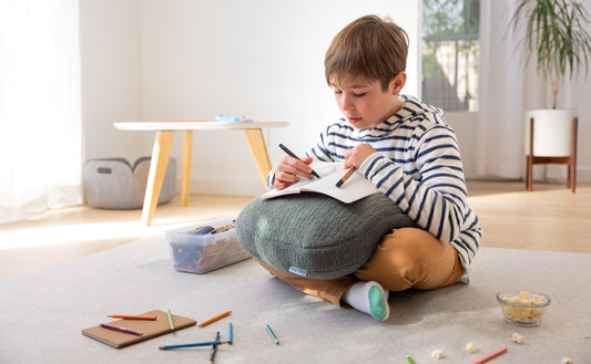 Child writing on a sage Quiet Mind weighted pillow during quiet playtime at home.