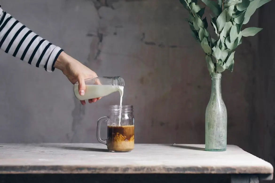 Person pouring milk into iced coffee mug to create an anxiety relief drink.