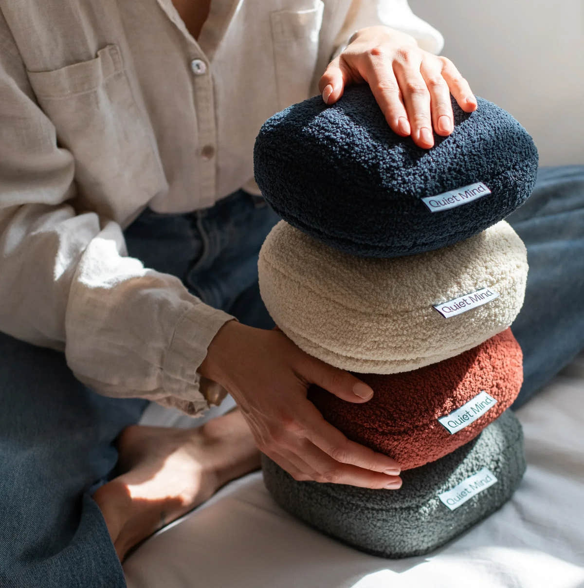 Stacked Quiet Mind weighted pillows in different colors held by a person for sensory comfort.