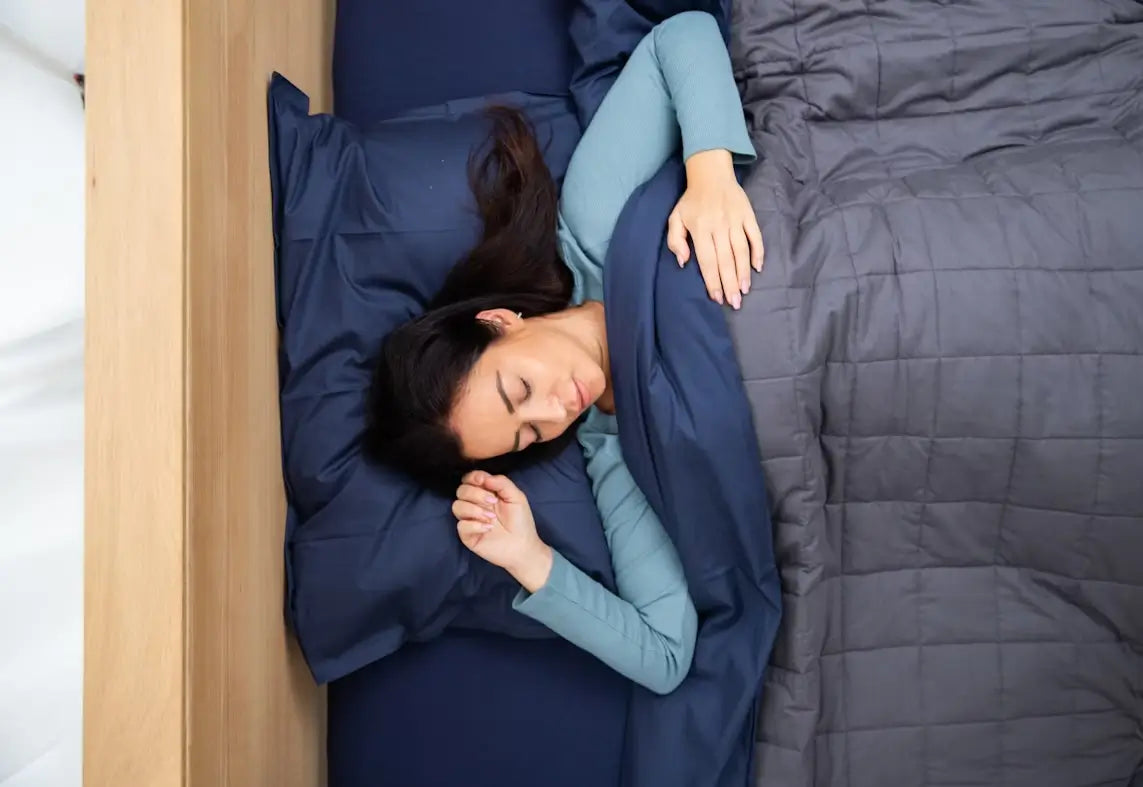Woman sleeping under a grey weighted blanket on navy bedding.