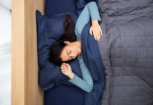 Woman sleeping under a grey weighted blanket on navy bedding.