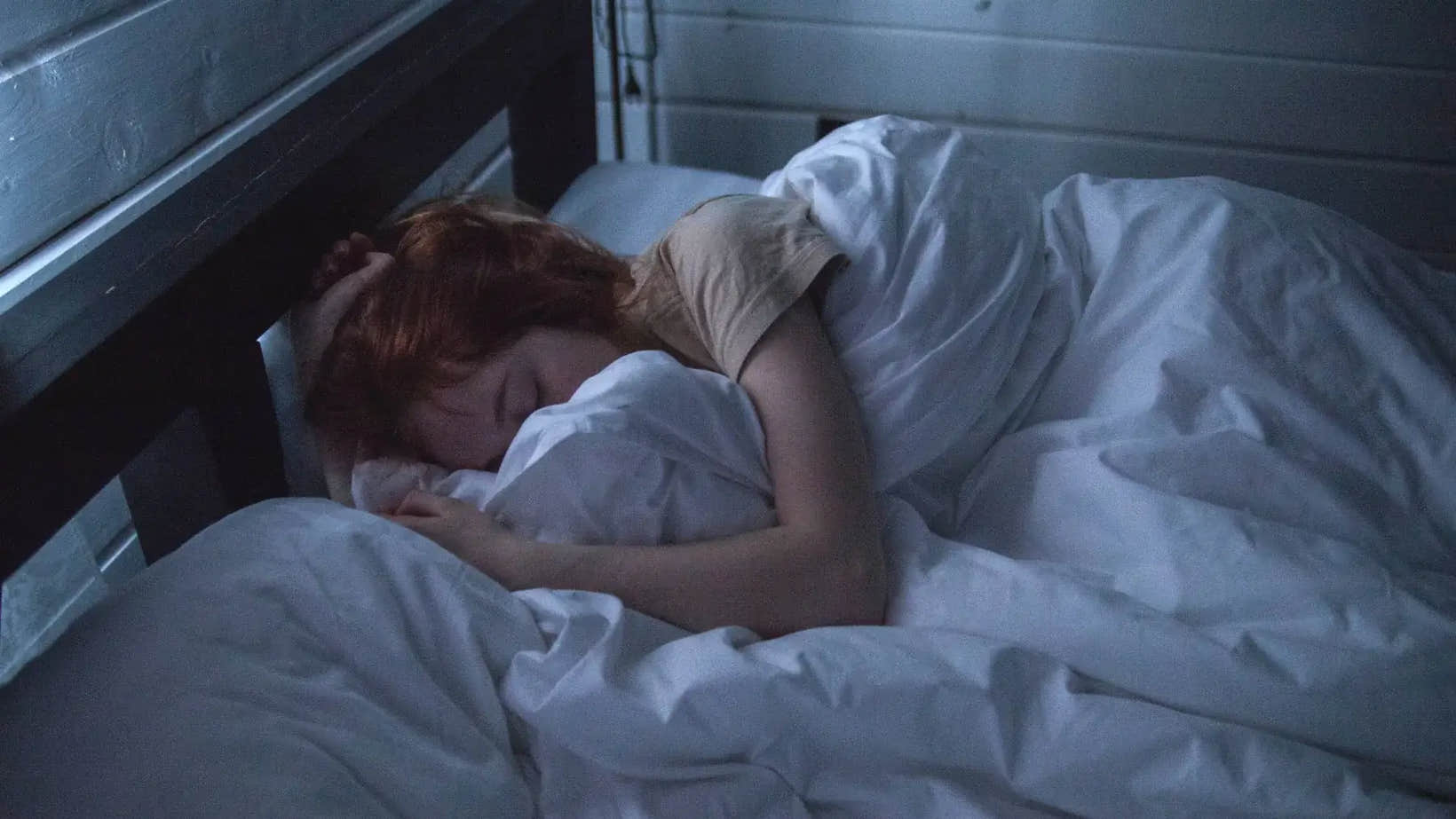 Person sleeping peacefully in a dimly lit room, curled up in bed.