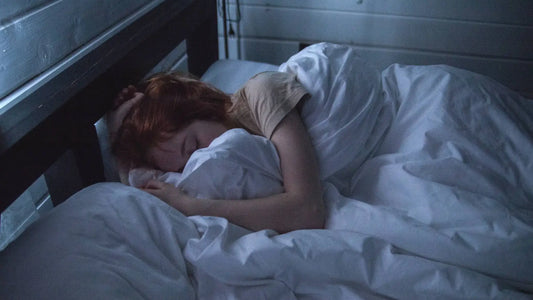 Person sleeping peacefully in a dimly lit room, curled up in bed.
