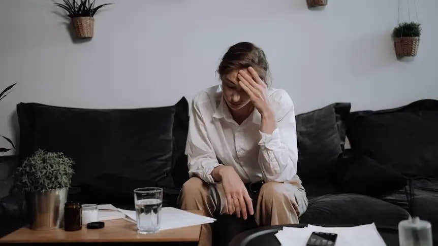 Stressed woman sitting on couch, holding head.