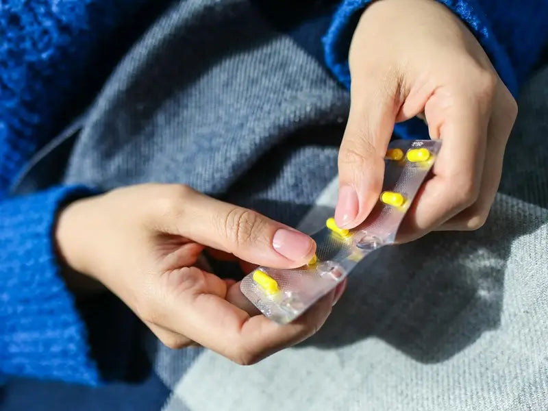 Close-up of a person holding a blister pack of yellow capsules.