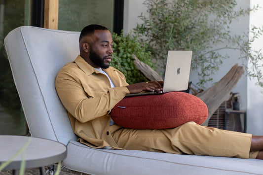 Man works on a laptop with a rust Quiet Mind weighted pillow across his lap.