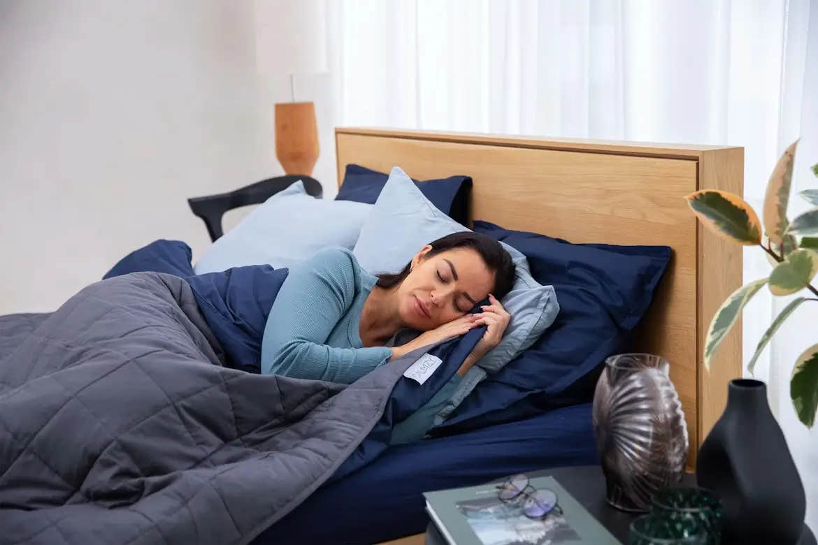 Woman peacefully sleeping in bed under a dark gray weighted blanket.