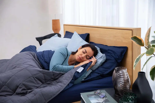 Woman peacefully sleeping in bed under a dark gray weighted blanket.