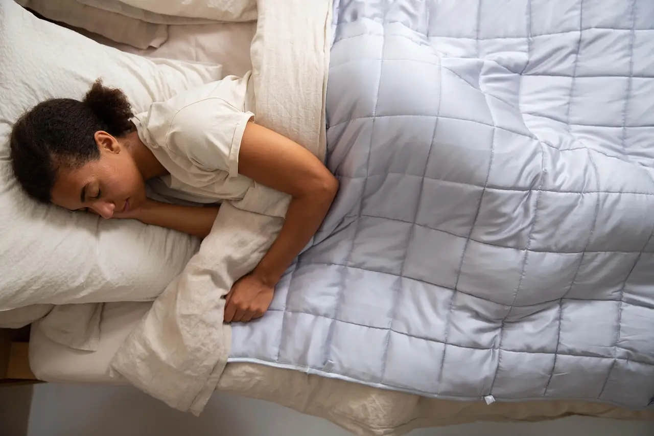 Woman sleeping peacefully on her side under a gray weighted blanket.