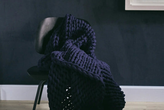  Dark chunky weighted blanket draped over a black chair in a minimalist room.