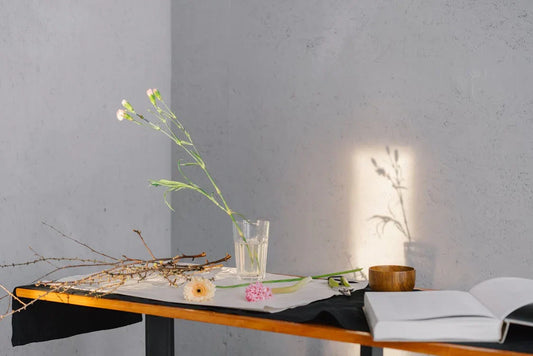 Minimal table with flowers, a glass of water, and an open book in soft sunlight.