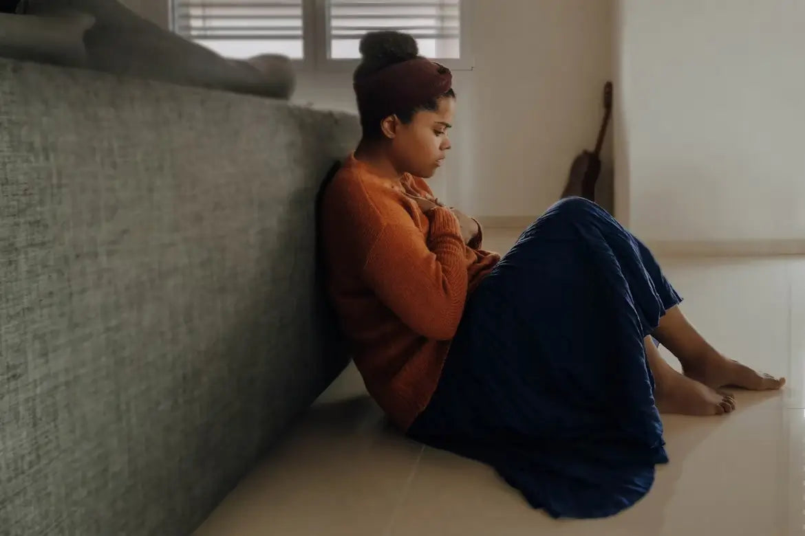 Woman sitting on the floor, holding her chest, appearing anxious.
