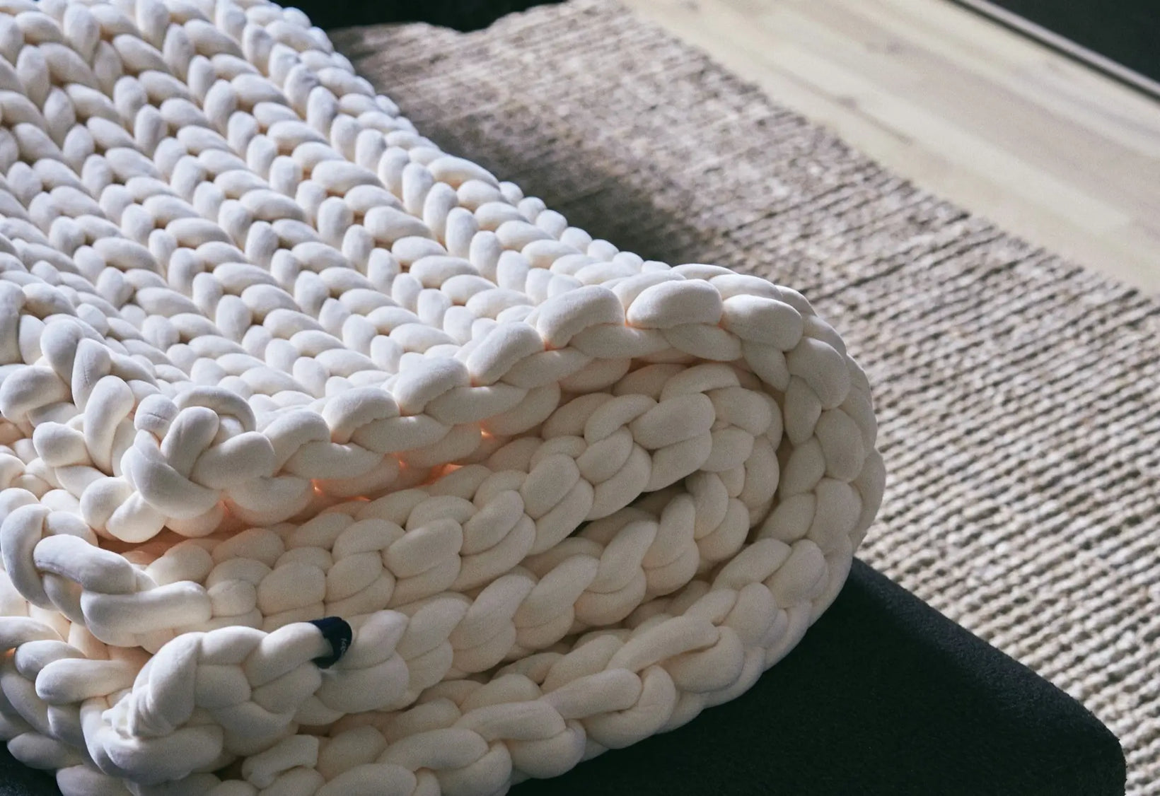Thick white chunky knit weighted blanket folded on wooden surface with textured mat.