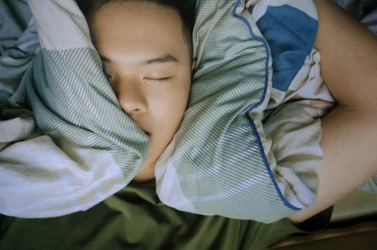 Person sleeping with face partially covered by a green striped blanket.