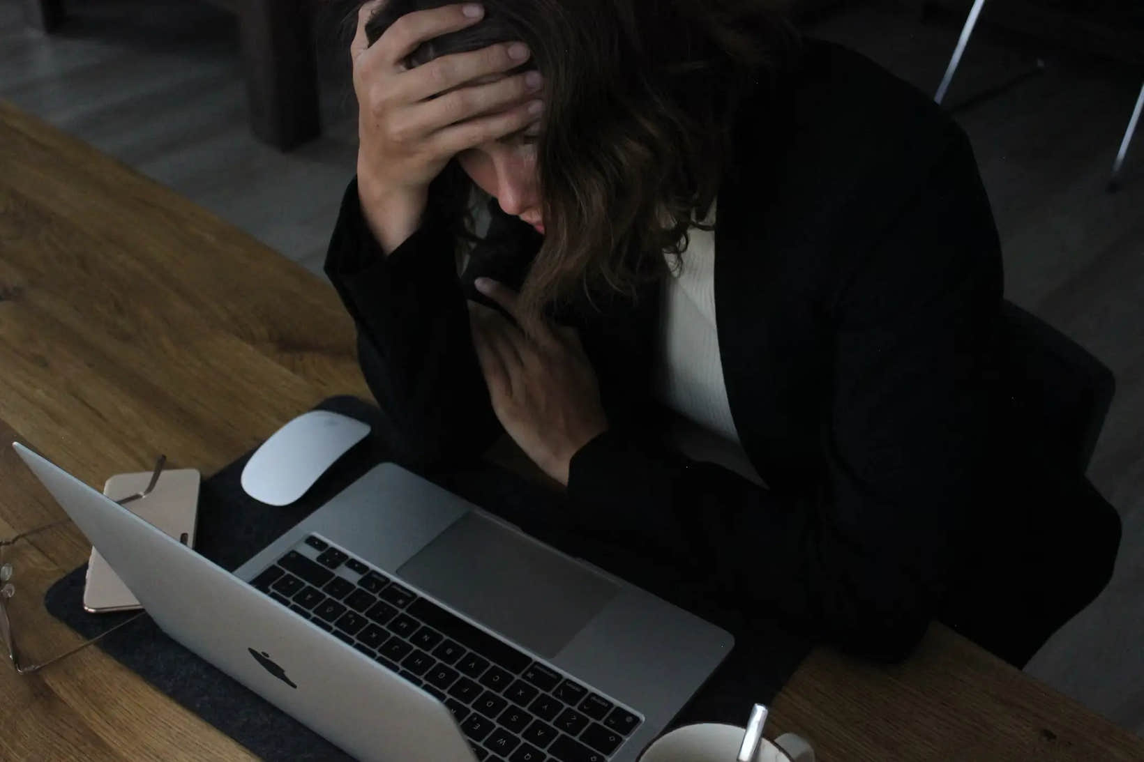 A woman sitting at a desk with her head in her hand, looking stressed while working on a laptop—illustrating the overwhelm that often comes with overthinking and chronic stress.