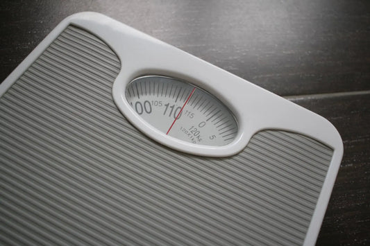 A close-up of a bathroom scale showing a reading around 110 kilograms, symbolizing weight gain—often linked to chronic stress, hormonal imbalance, and emotional eating patterns.