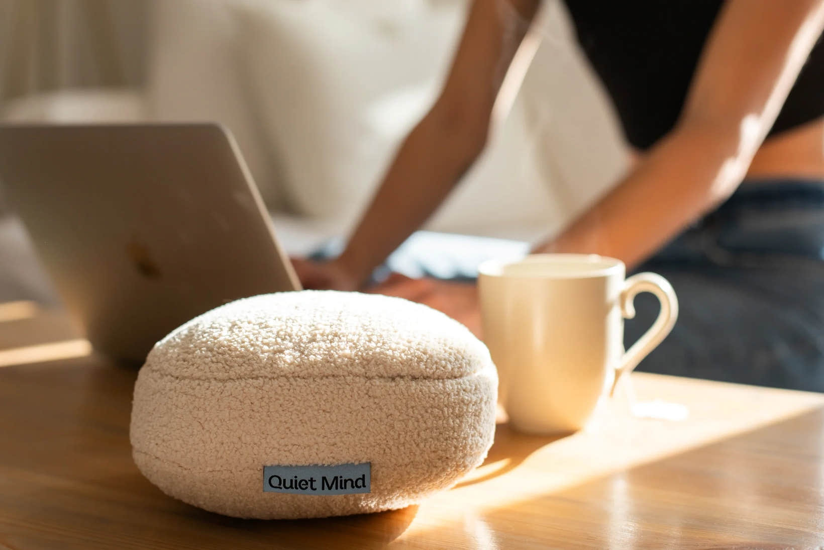 Cream Quiet Mind weighted stress ball sits beside a laptop and mug on a sunlit desk.