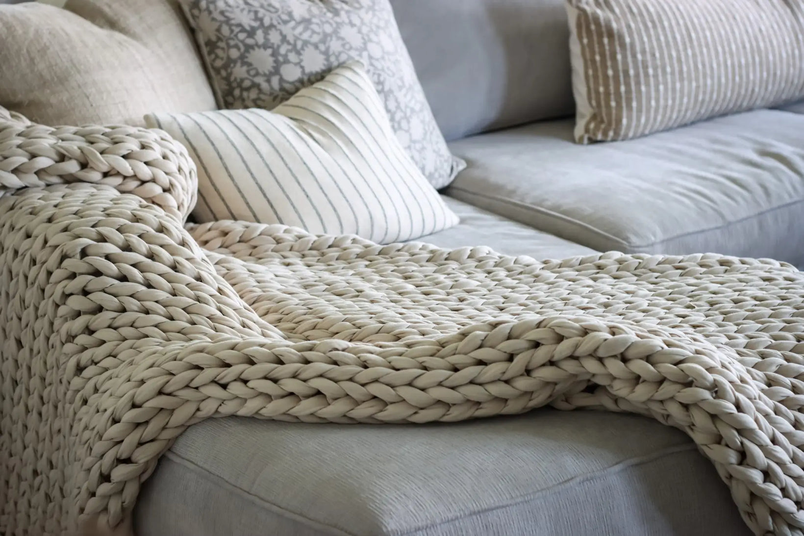 A chunky knit weighted blanket draped over a cozy couch with neutral throw pillows.