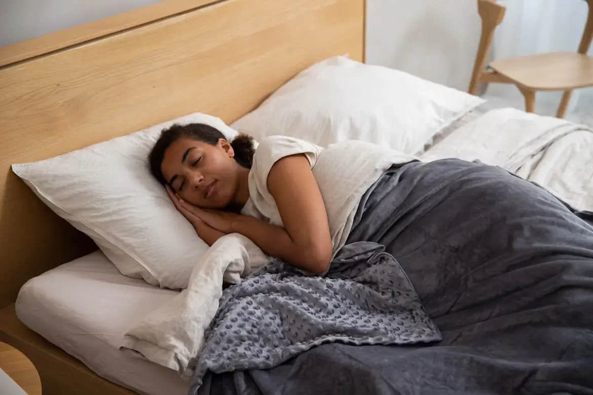 Woman sleeping under a gray weighted blanket on a bed.