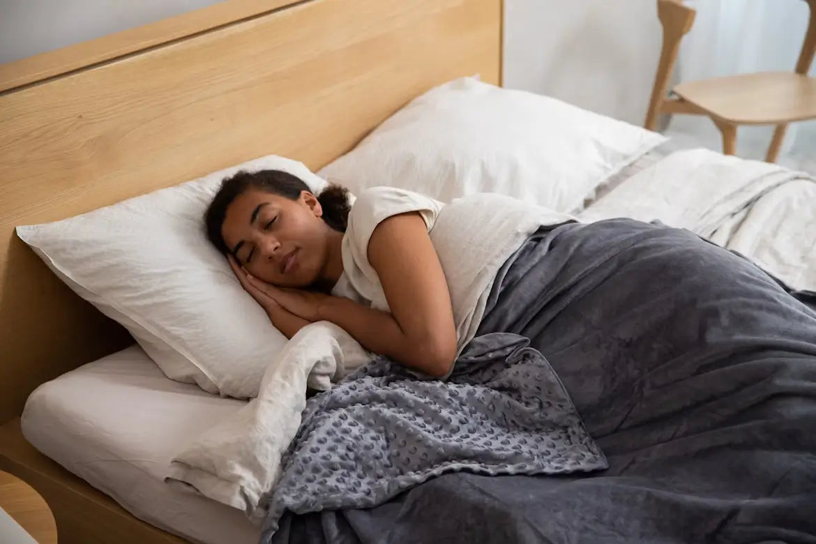 Woman sleeping under a gray weighted blanket on a bed.