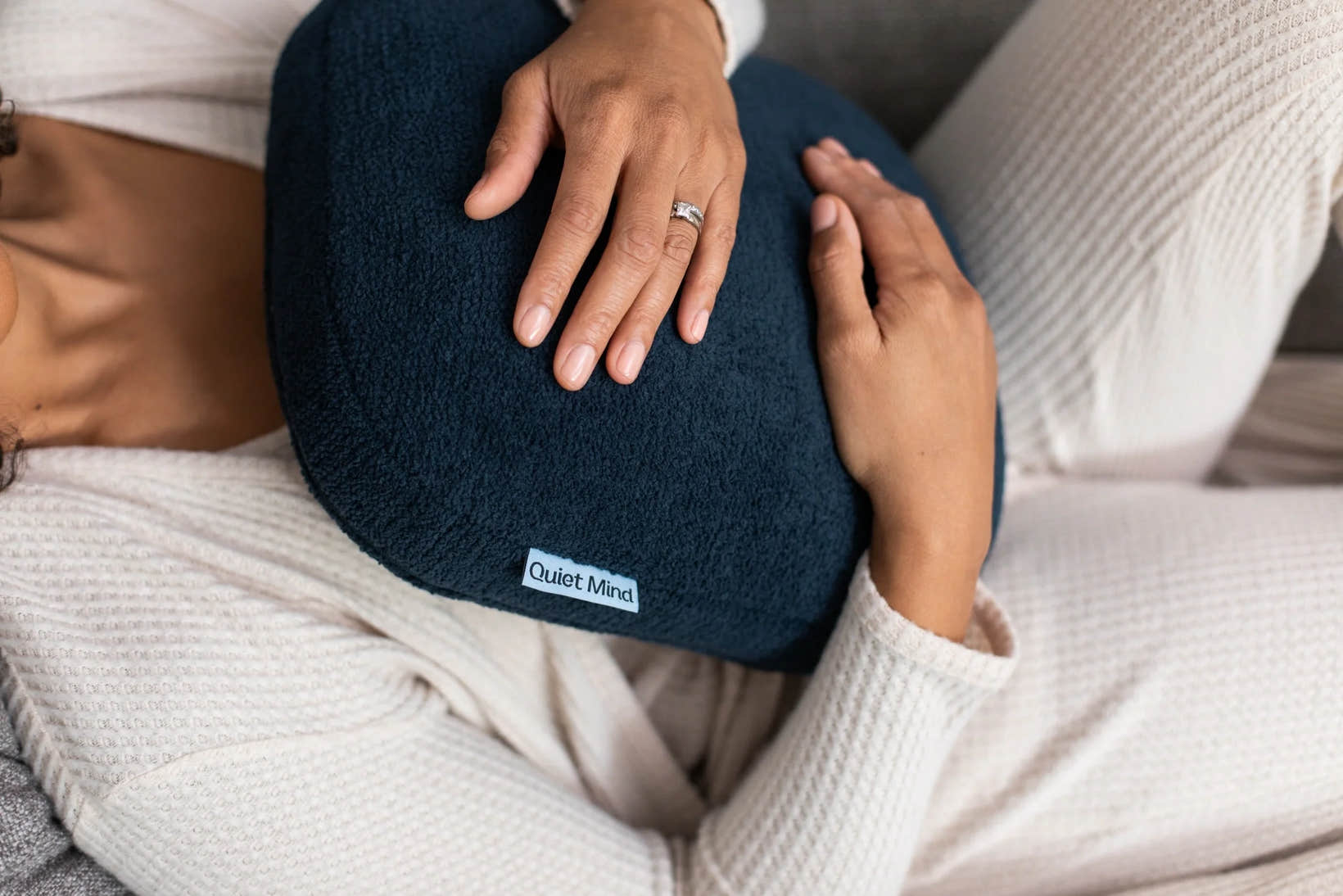 Person reclines on a sofa while holding a navy Quiet Mind weighted pillow.