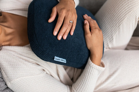 Person reclines on a sofa while holding a navy Quiet Mind weighted pillow.