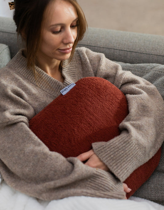Woman hugging a rust Quiet Mind weighted pillow while relaxing on a gray sofa.
