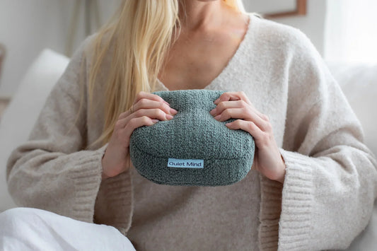Woman holds a green Quiet Mind weighted stress ball with both hands.
