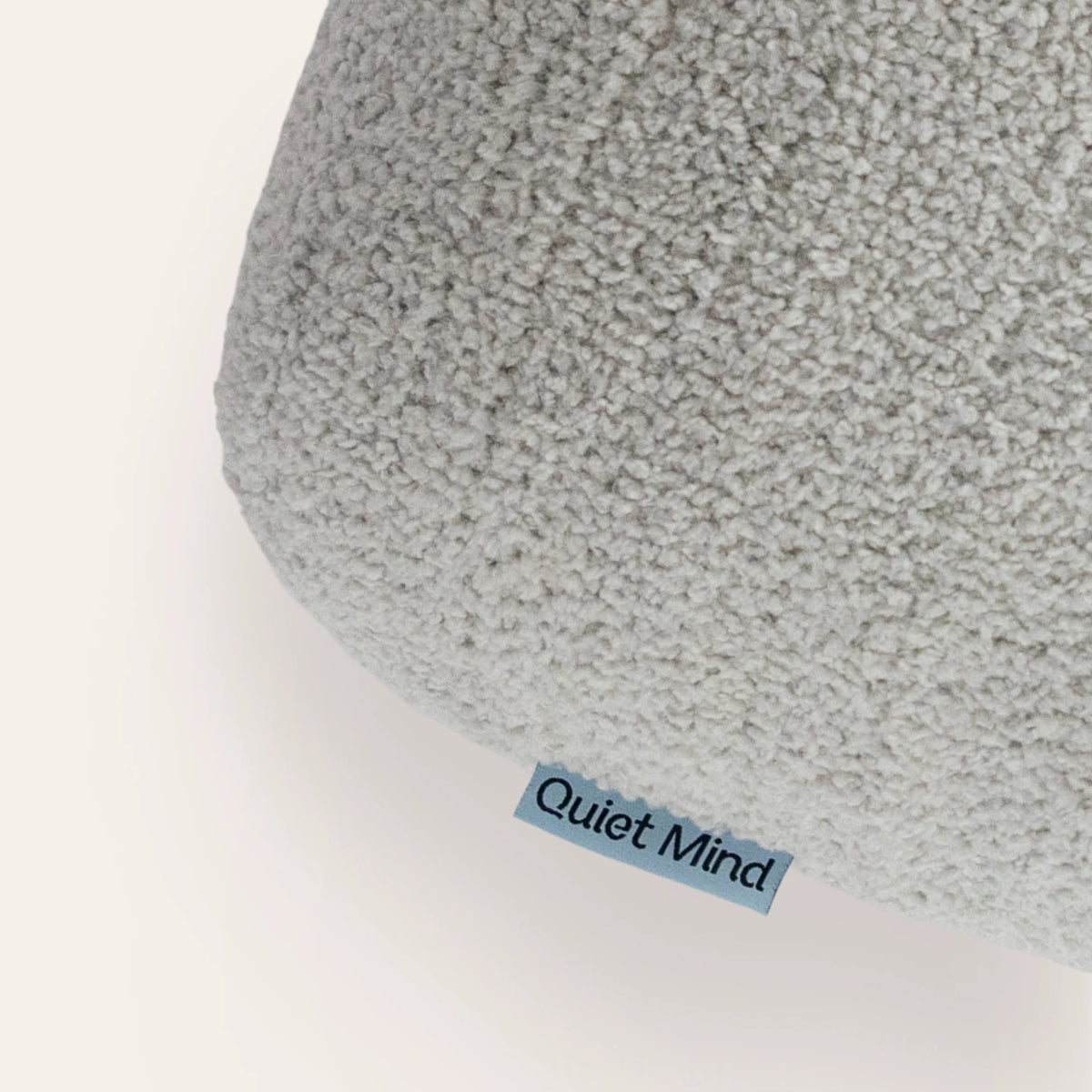 Close-up of a light gray textured plush cushion with a small blue tag reading 'Quiet Mind' on a white background.