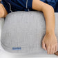 A person lying in bed with their head resting on a large, textured gray pillow. The person is wearing navy blue pajamas with white piping, and the pillow features a small blue label that reads 'Quiet Mind'.